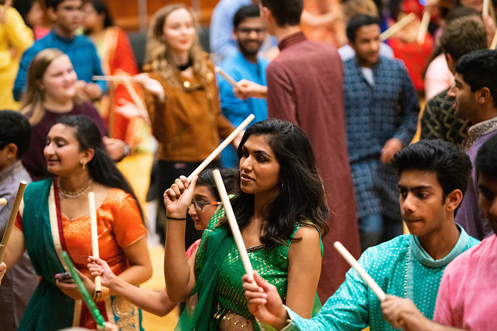 Students dancing and holding wooden sticks as part of GRBB: Garba. Raas. Bollywood. Bhangra