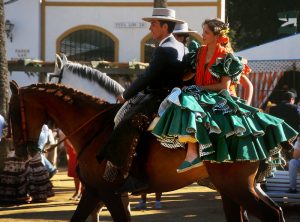 A picture showing a men and a woman riding a horse wearing traditional clothes