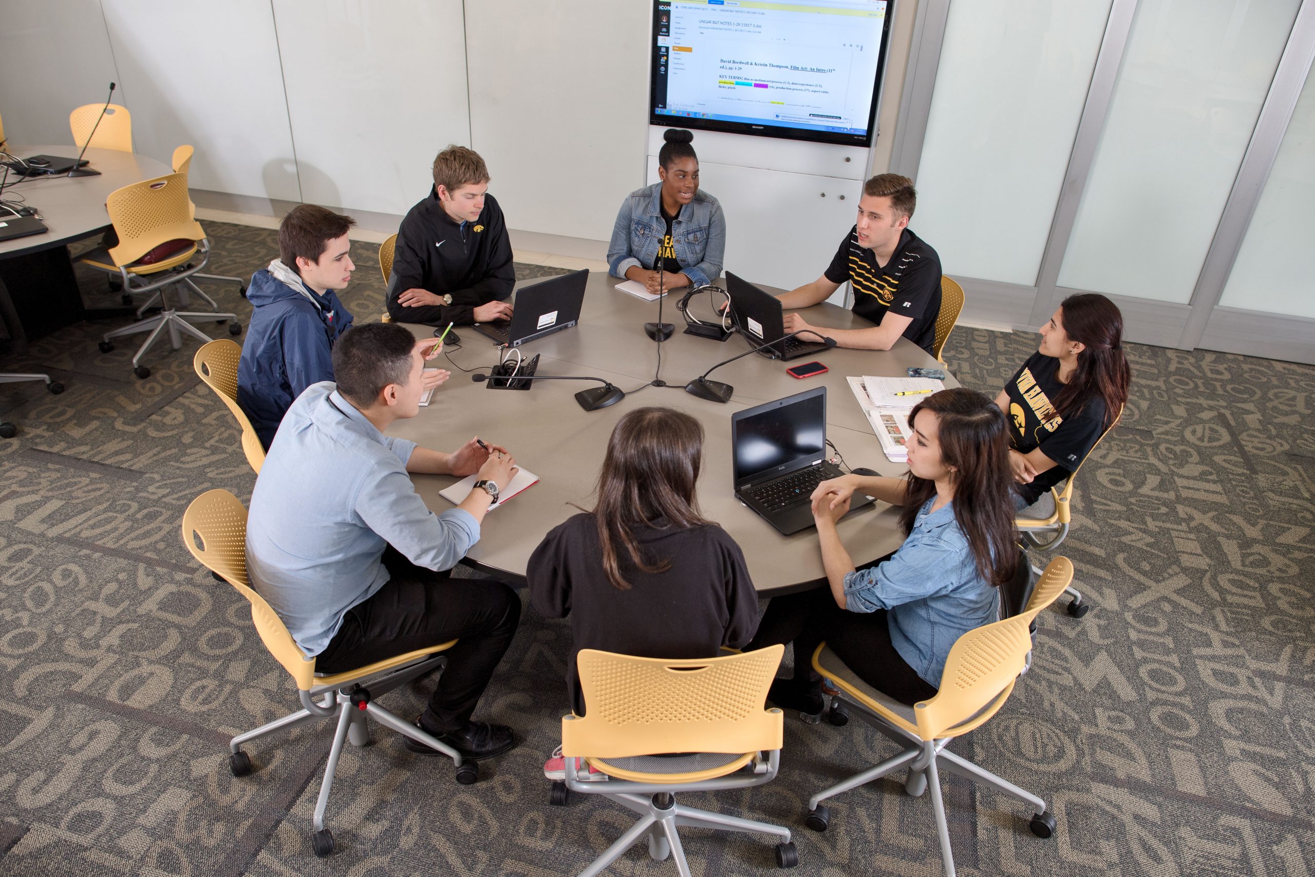 A group of eight students working together at a round table in an active learning classroom.