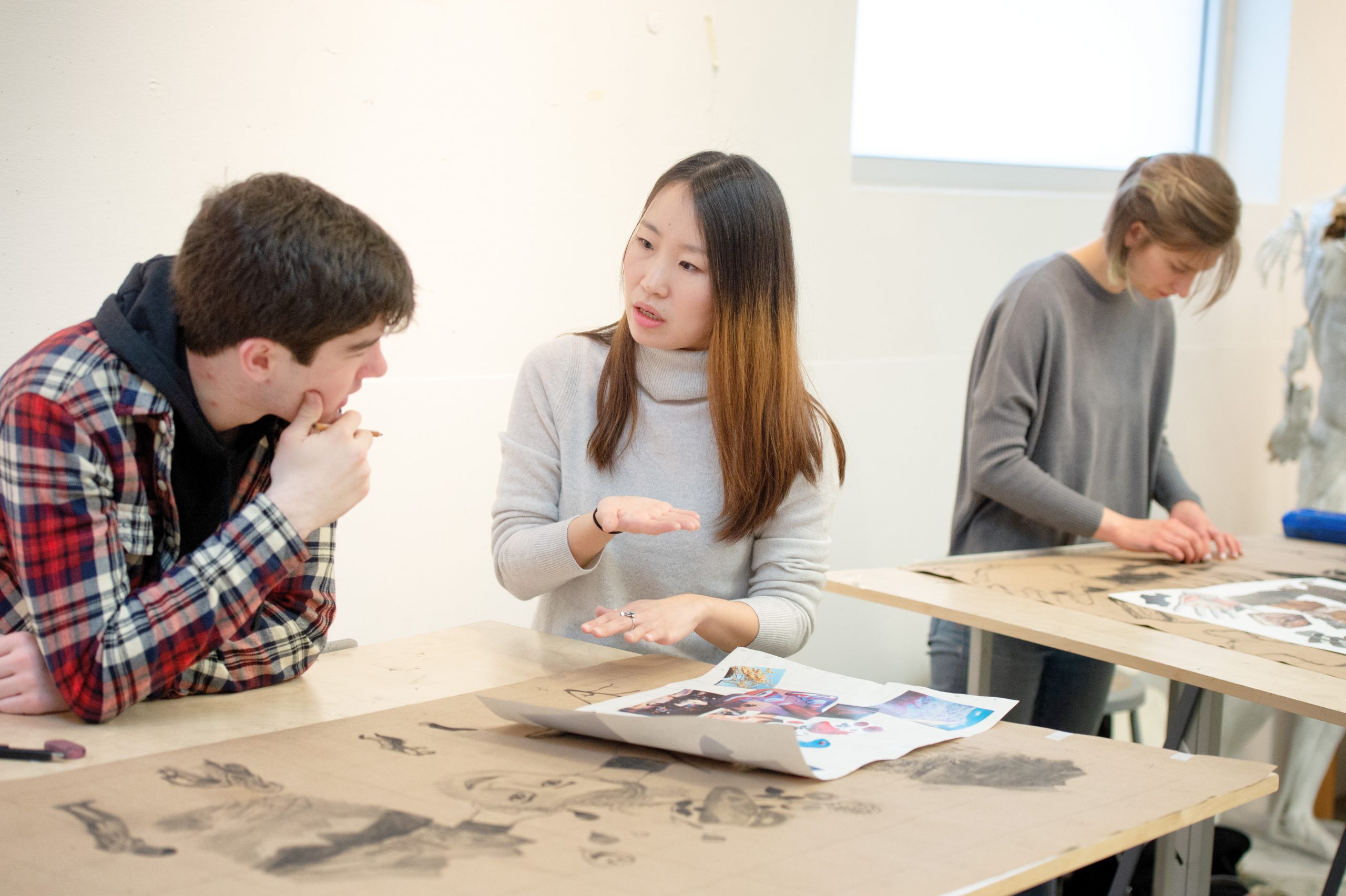 Instructor YooJung Hong giving feedback to a student working on a large charcoal drawing.