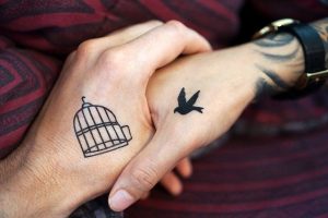 A tattoo of a bird and a cage show on two holding hands