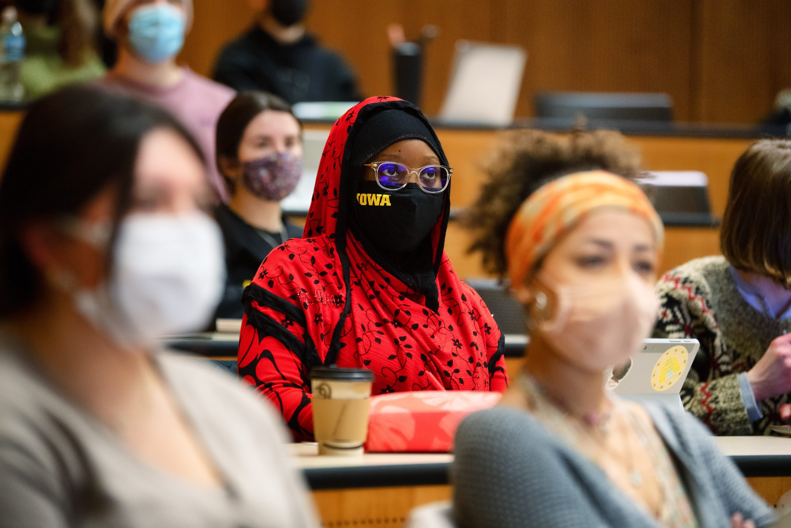 A group of students wearing masks sitting in a large lecture hall.