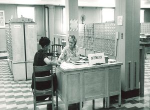 Black and white photo of two women sitting at a wooden desk with card catalogs in the background.