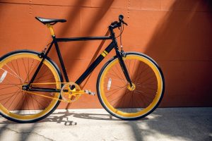A stylish black and yellow bicycle leaning against an orange wall, with sunlight casting shadows on the ground.
