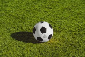 A black and white soccer ball resting on a vibrant green grass field, casting a shadow.