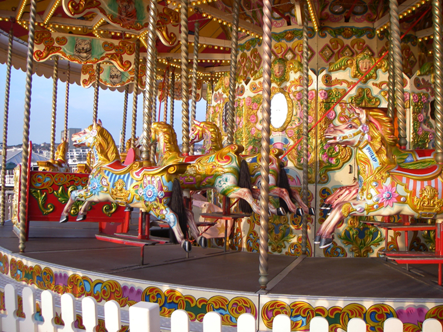 The figure shows a clock-wise rotating empty merry go round with iron bars holding the decorated wooden horse statues, four in each column.