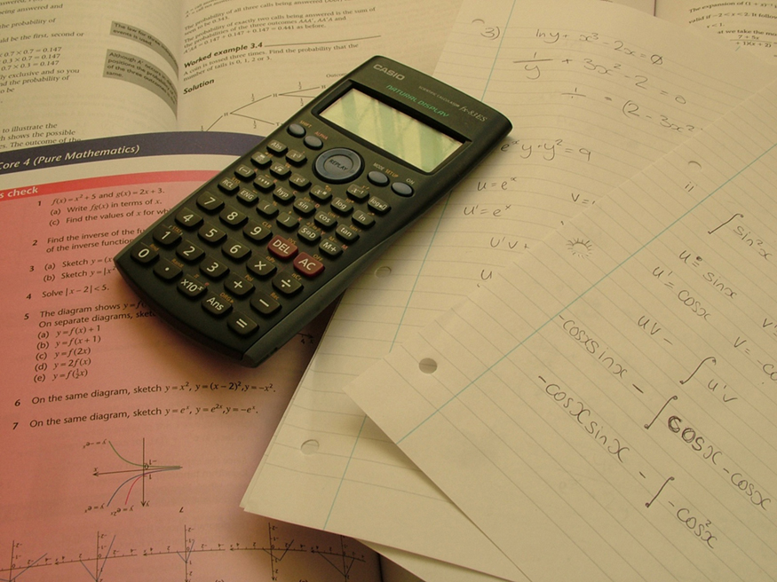 A calculator is placed on open math books and few papers. Problems on trigonometry are solved on one of the papers.