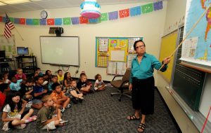 A teacher points to a map in front of elementary school students in a classroom