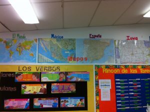 A classroom's wall with the map of the world, Spain, Mexico, and Iowa,